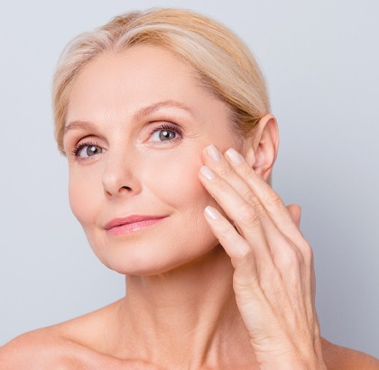 Older mature woman feeling her cheek with hand, smooth skin on her face